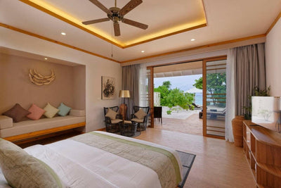 A Beach Villa bedroom at Brennia Kottefaru, a sofa under the window and doors to the garden