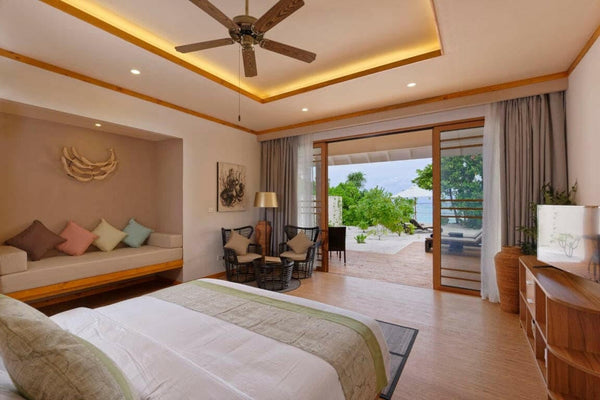 A Beach Villa bedroom at Brennia Kottefaru, a sofa under the window and doors to the garden