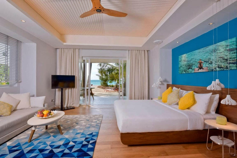 A villa room at Kandima Maldives, yellow cushions on the bed and reef photographs on a blue wall.
