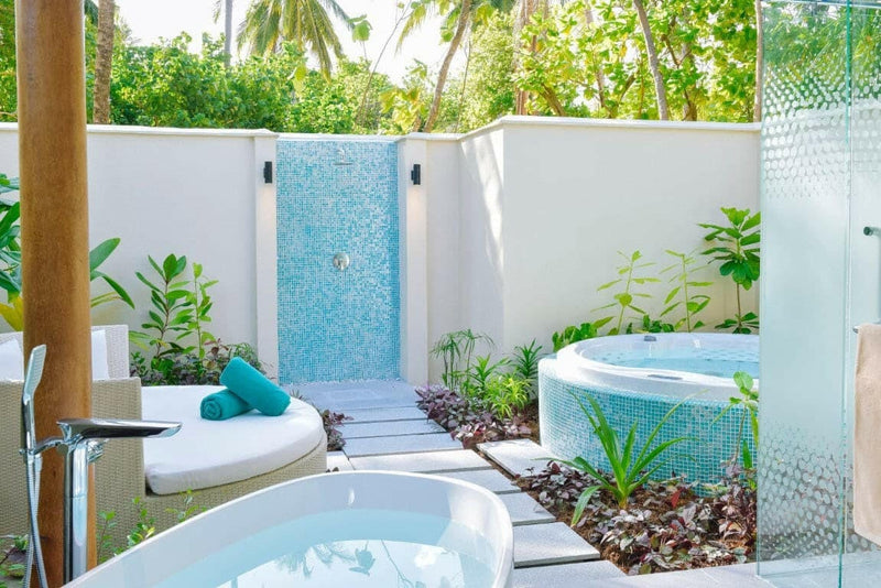 An open-air bathroom at Kandima Maldives, round tubs and a turquoise mosaic shower among planting.