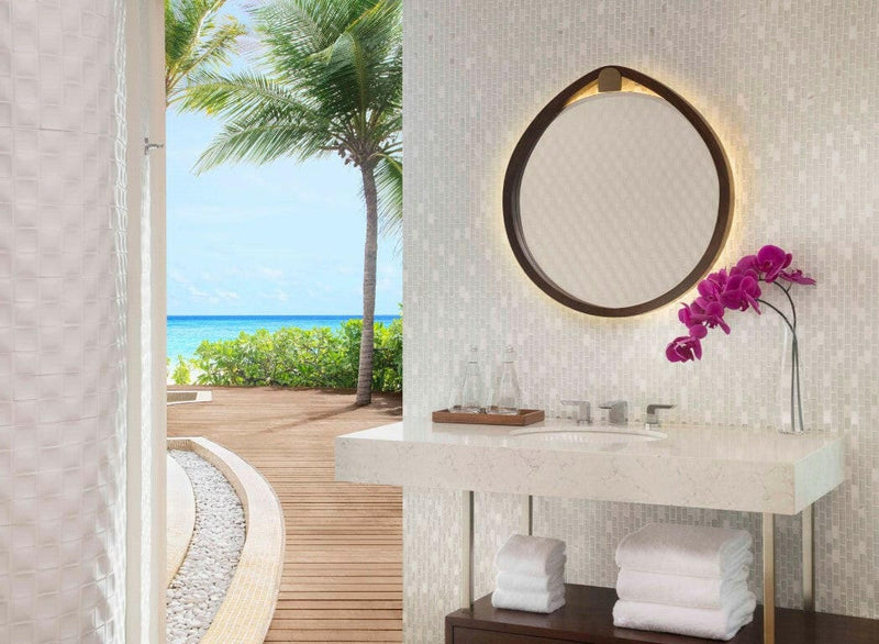 A villa vanity at JW Marriott Maldives, magenta orchids beside a backlit mirror, palms on the deck outside.