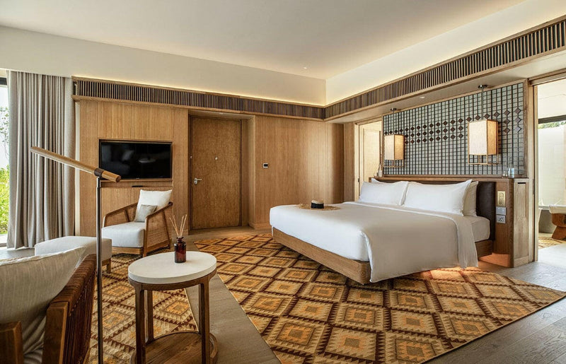 A bedroom at Kuda Villingili, white bed below two lantern sconces on a patterned headboard wall.