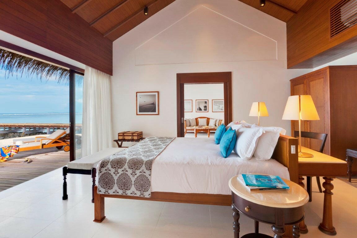A Beach Villa bedroom at The Residence Maldives at Falhumaafushi, teal cushions on the bed and a writing desk under the window