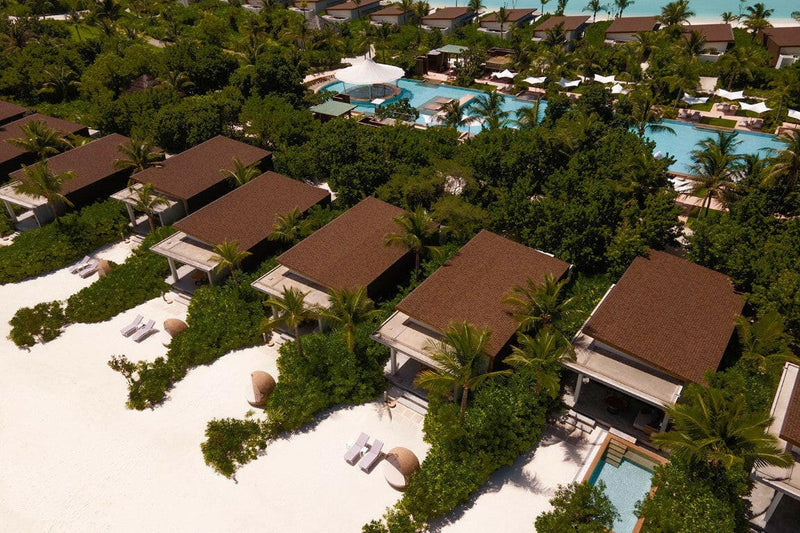 Kuda Villingili from the air, a row of pitched-roof beach villas behind white sand and loungers.