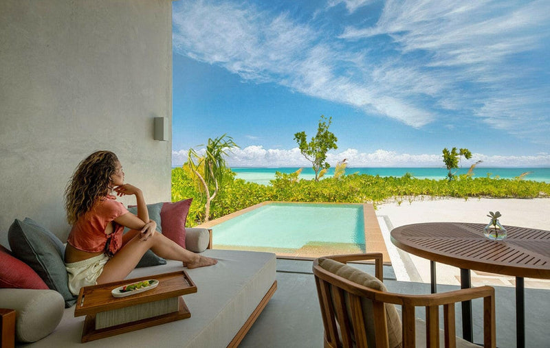 A guest reading on a daybed beside a villa pool at Kuda Villingili, timber table and chairs alongside.