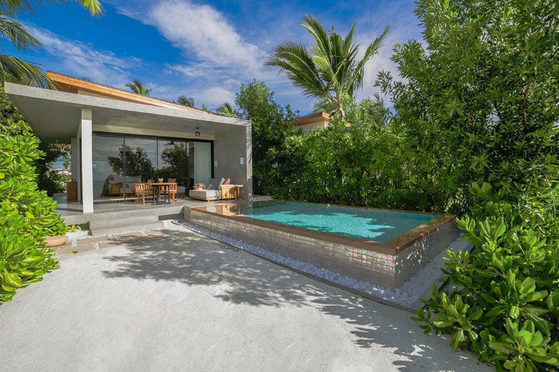 A raised pool outside a beach villa at Kuda Villingili, white sand and thick green shrubs around it.