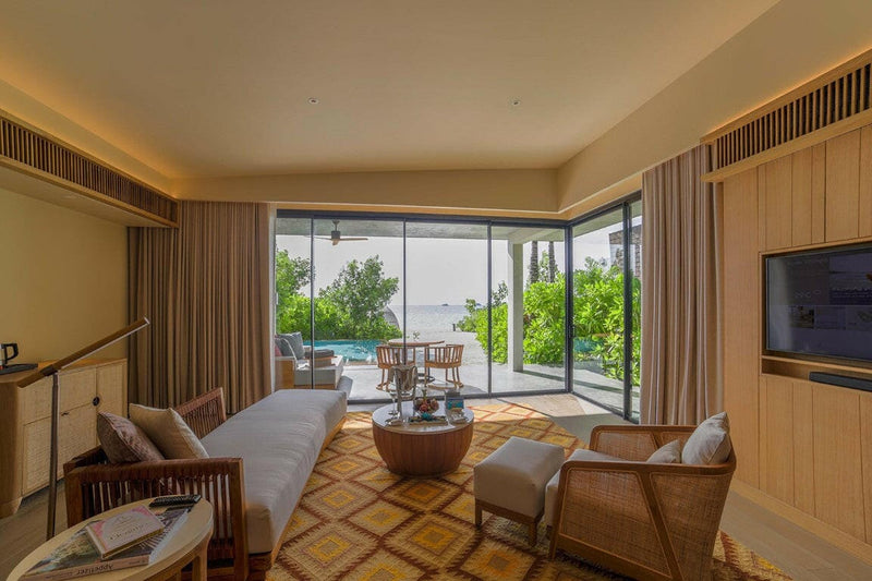 A villa living area at Kuda Villingili, armchairs on a yellow patterned rug facing the sea doors.