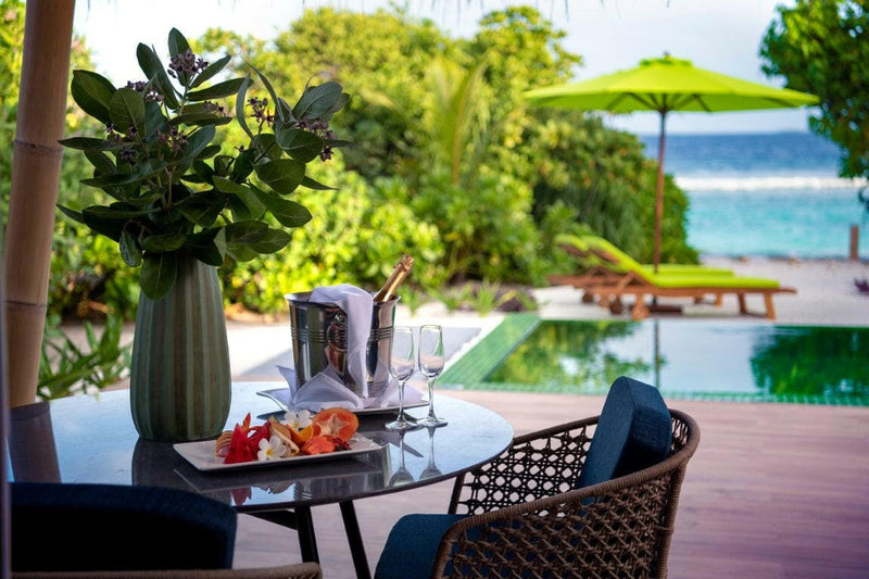 A deck table at Emerald Maldives, fruit and a wine cooler set beside a pool and lime parasol.