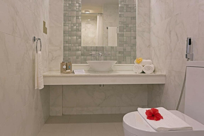 A tiled bathroom at Malahini Kuda Bandos with a vessel basin, mirror, walk-in shower and folded towels.