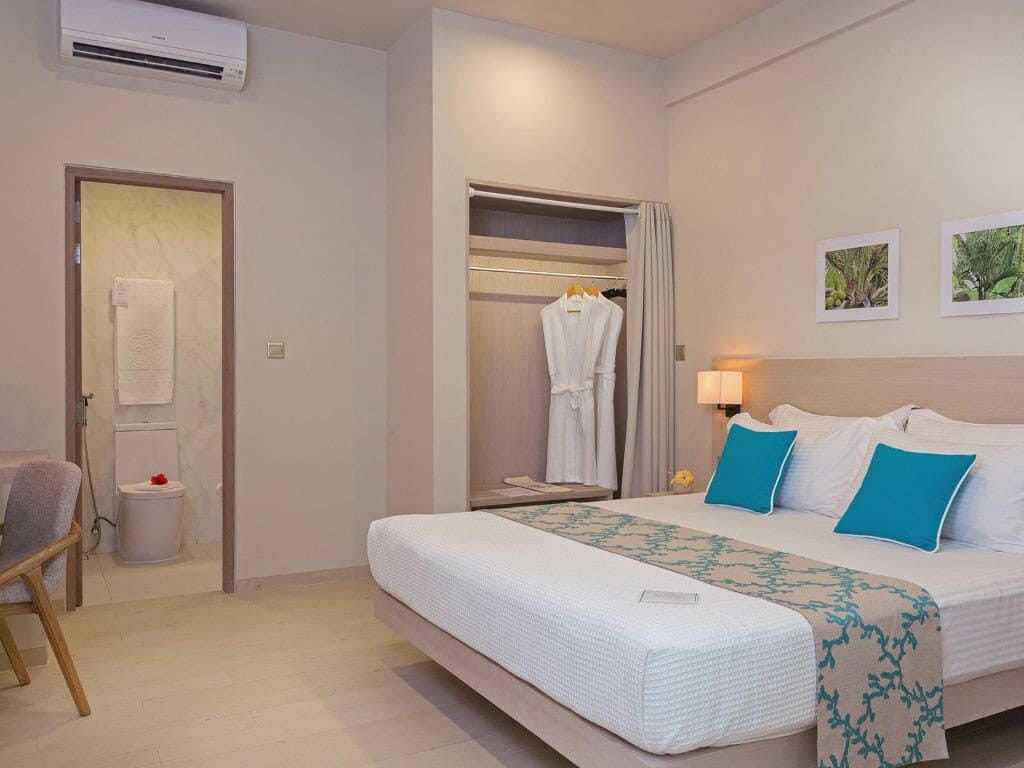 Malahini Kuda Bandos, North Malé Atoll — Garden Room with a king bed, an open wardrobe holding robes and the ensuite doorway beyond