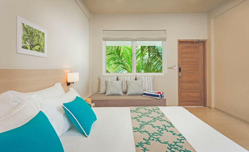 A Garden Room at Malahini Kuda Bandos with a king bed and a cushioned window seat under a window onto palms.