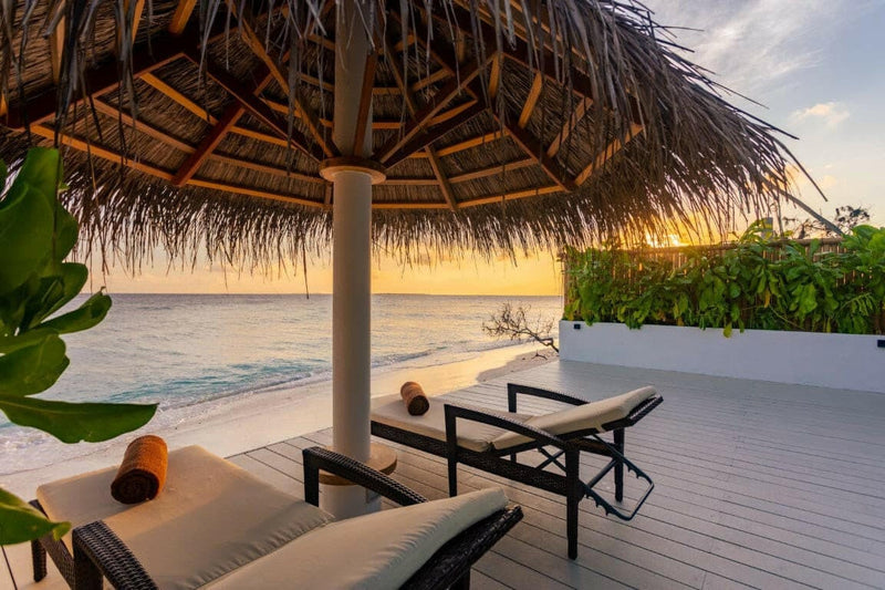 Sunset over the lagoon at Malahini Kuda Bandos from a deck with two sun loungers under a thatched parasol.