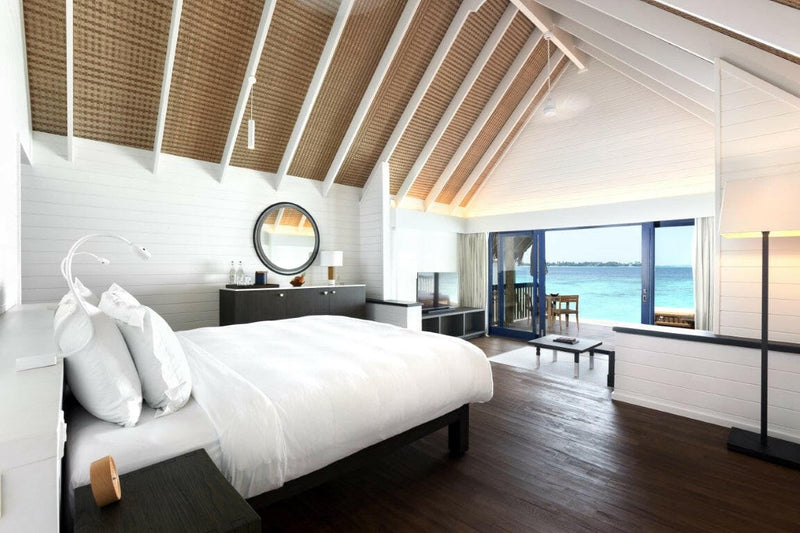 A Dhoni Water Villa bedroom at COMO Cocoa Island, a white bed under a pitched timber ceiling