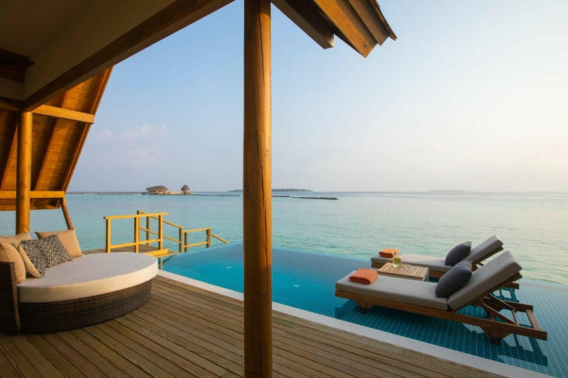 The deck of a water villa at Emerald Faarufushi, a daybed and loungers beside the pool above the lagoon