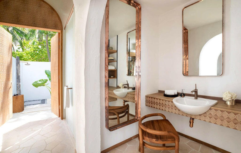 A villa bathroom at Sirru Fen Fushi, copper framed mirrors above a woven vanity, courtyard outside.