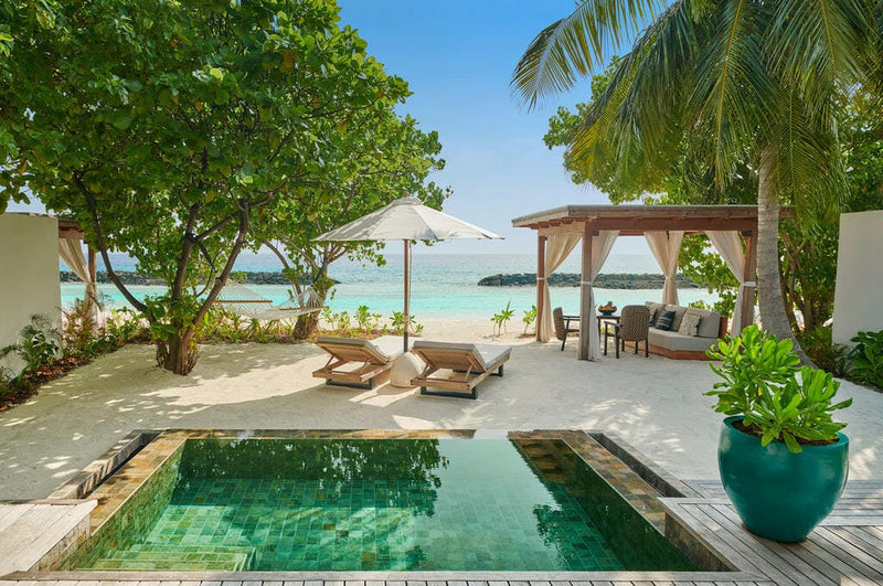 A beach villa pool at Sirru Fen Fushi, dark tiled water and loungers under a shaded pergola.