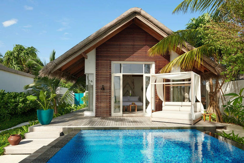 A beach villa at Sirru Fen Fushi, long blue pool in front of a timber gable and canopied daybed.