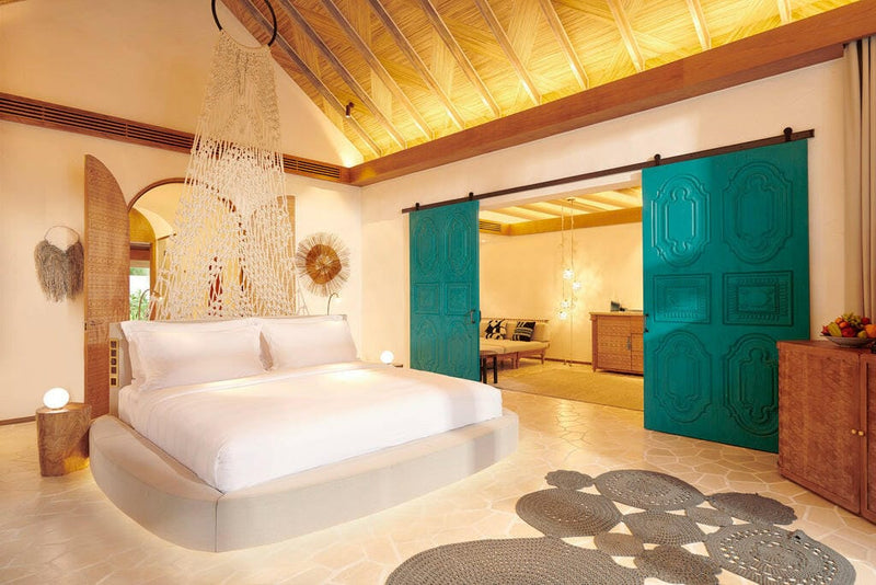 A villa bedroom at Sirru Fen Fushi, tall woven pendant above the bed beside green carved doors.
