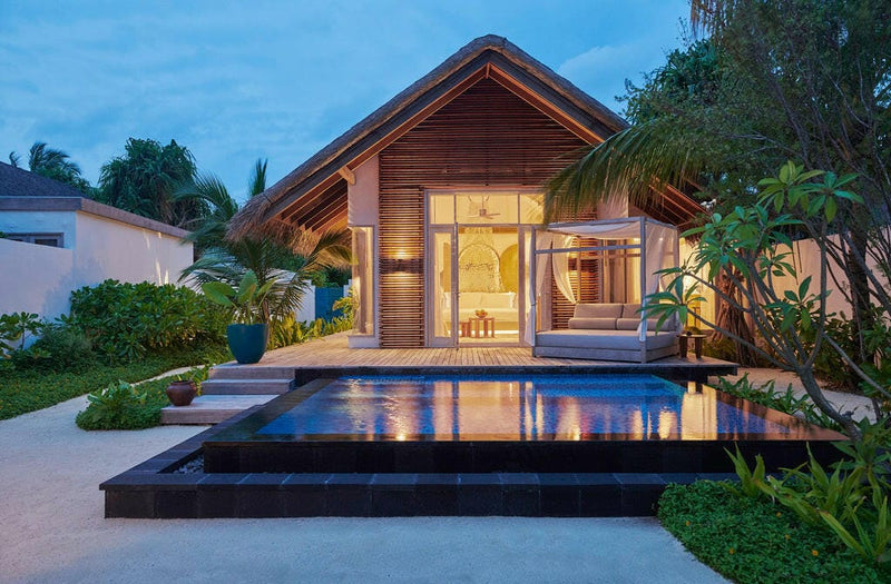 A beach villa at Sirru Fen Fushi at dusk, warm light inside and a pool reflecting the gable.