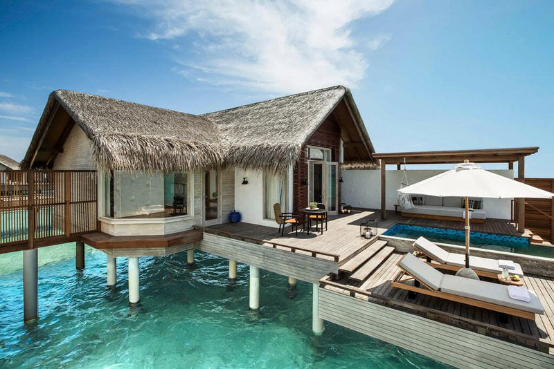 A water villa at Sirru Fen Fushi, thatched roof above a deck pool and loungers on stilts.