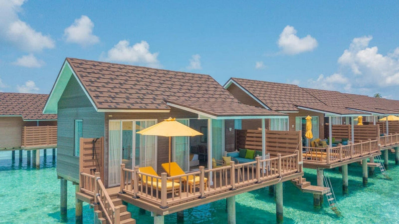 Water villas at Dhigufaru Island Resort, yellow parasols on stilted decks above turquoise shallows.