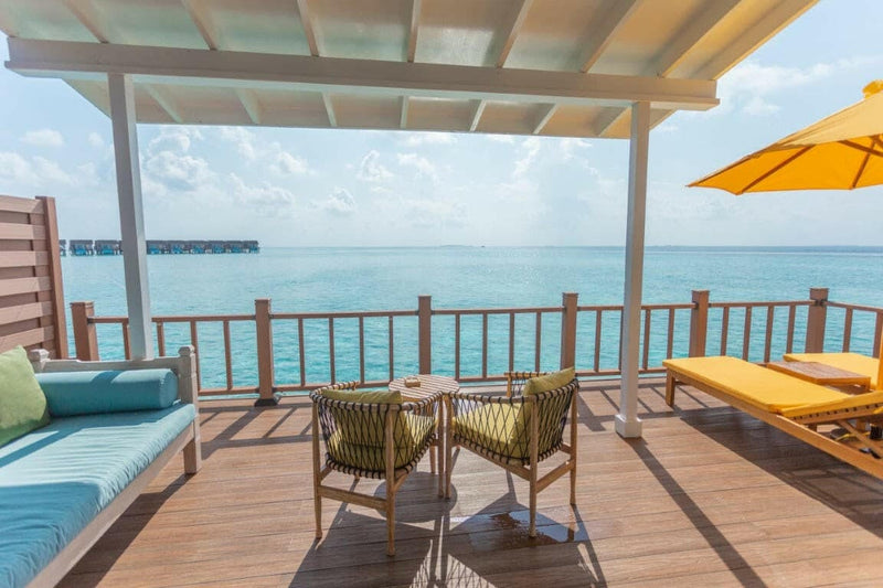 A water villa deck at Dhigufaru Island Resort, woven armchairs and a yellow lounger facing the lagoon.
