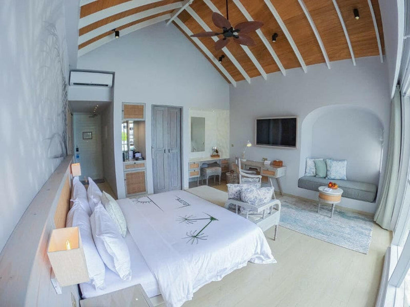 A suite interior at Malahini Kuda Bandos with a timber vaulted ceiling, ceiling fans, sofa and writing desk.
