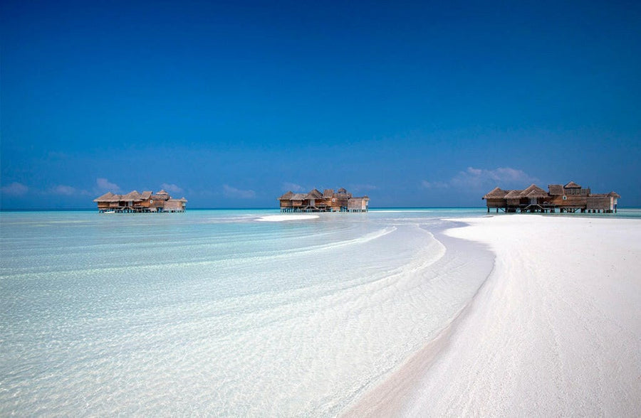 A curving sandbank at Gili Lankanfushi, pale shallows and overwater villas along the horizon.