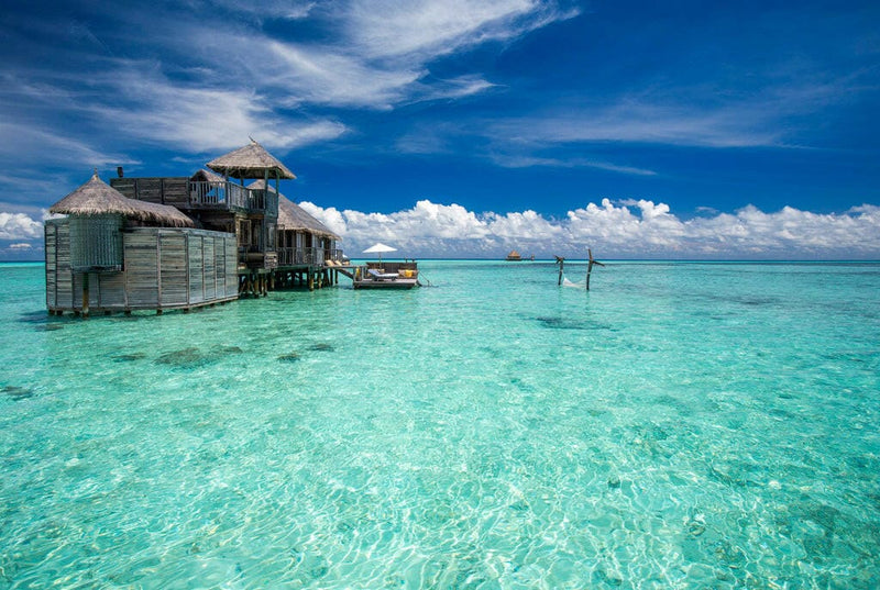 A timber residence on stilts at Gili Lankanfushi, standing out over the shallow lagoon at the end of a jetty