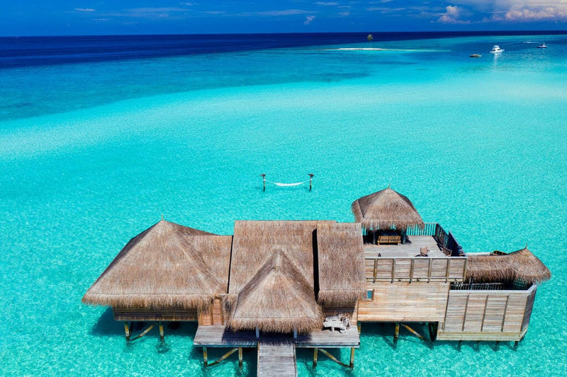 Gili Lankanfushi from above, thatched villas linked by timber jetties over bright turquoise water.