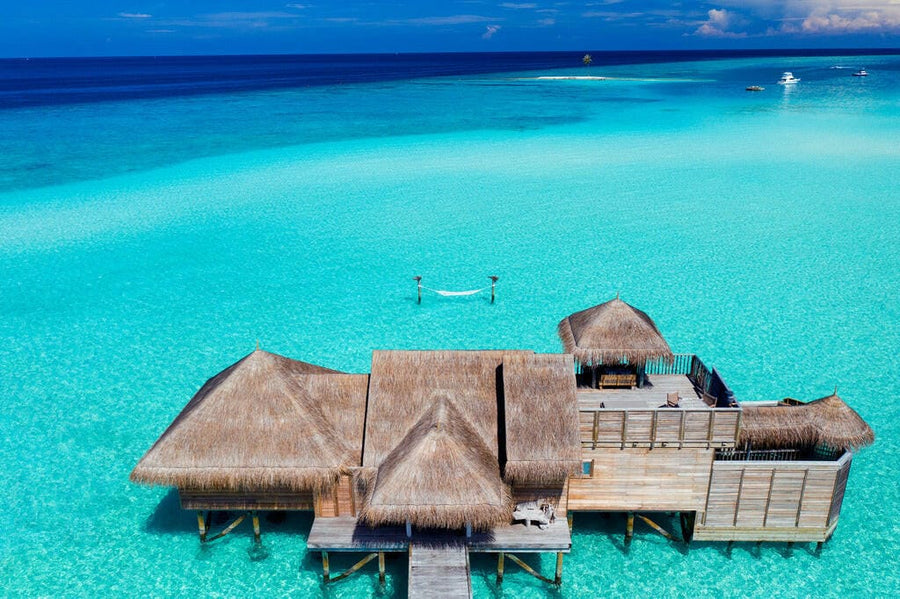 Gili Lankanfushi from above, thatched villas linked by timber jetties over bright turquoise water.