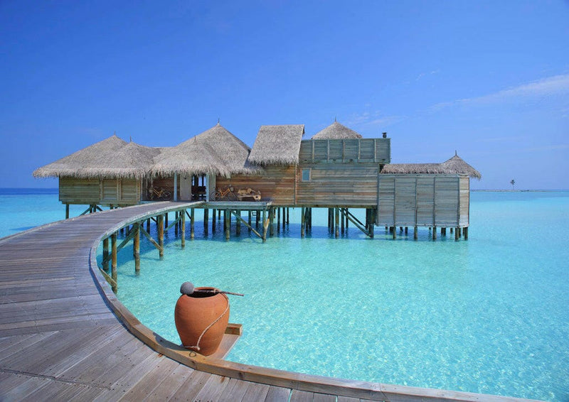 A curving timber jetty at Gili Lankanfushi with a terracotta pot, leading to villas on stilts.
