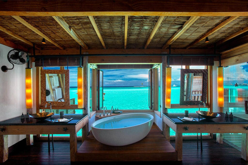 A villa bathroom at Gili Lankanfushi, oval freestanding tub between twin timber-framed mirrors.