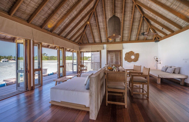 An open-plan residence at Gili Lankanfushi, bed, dining table and glass doors onto the deck.