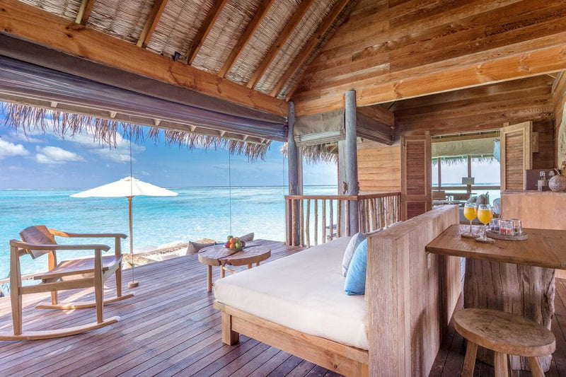 A villa bedroom at Gili Lankanfushi looking out to a deck with a white parasol and the lagoon.