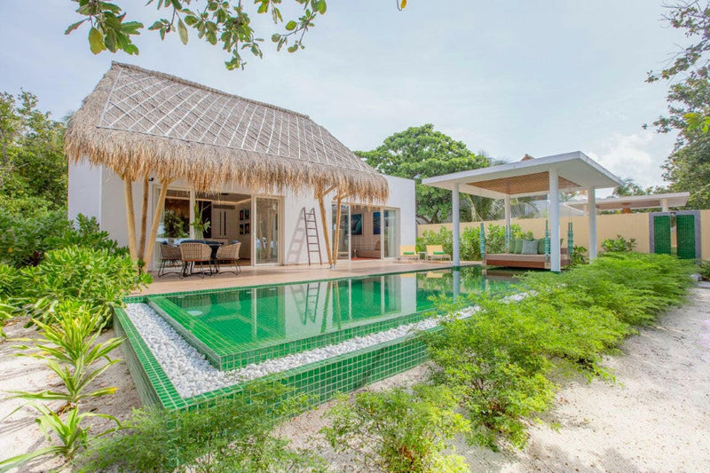 A beach villa at Emerald Maldives, lounger on the deck beside a green tiled pool in the garden.