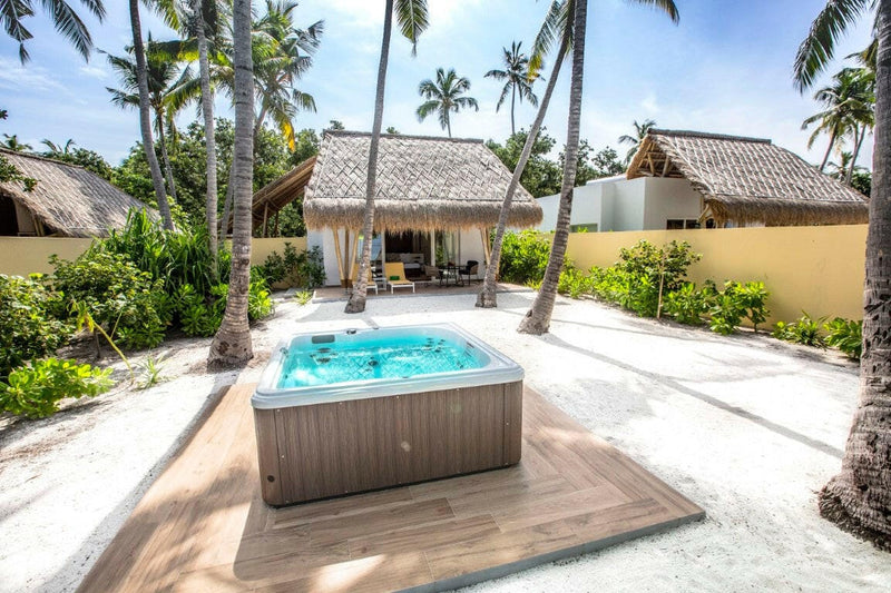 A sunken hot tub at Emerald Maldives, square jacuzzi in timber decking inside a walled palm garden.