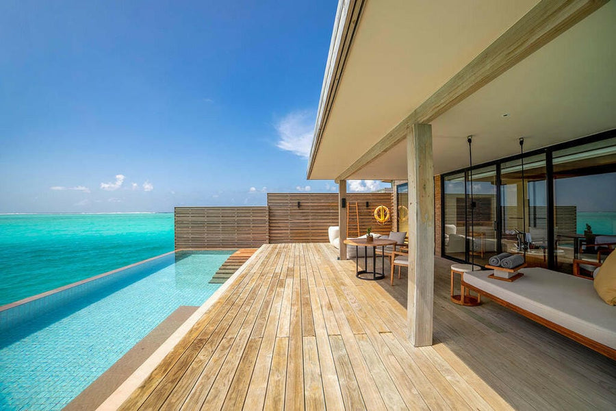 The deck of a water villa at Kuda Villingili, long infinity pool beside a shaded daybed.