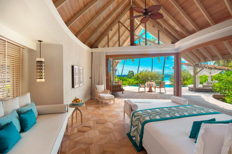 A beach villa bedroom at Milaidhoo Maldives, teal cushions under a high timber vaulted ceiling.