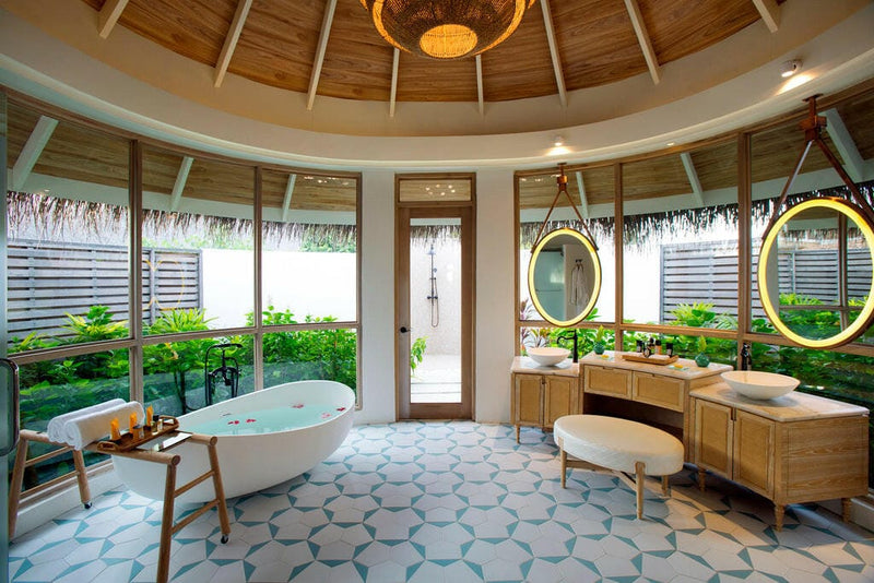 A villa bathroom at Milaidhoo Maldives, oval tub and twin gold mirrors on patterned green tiles.