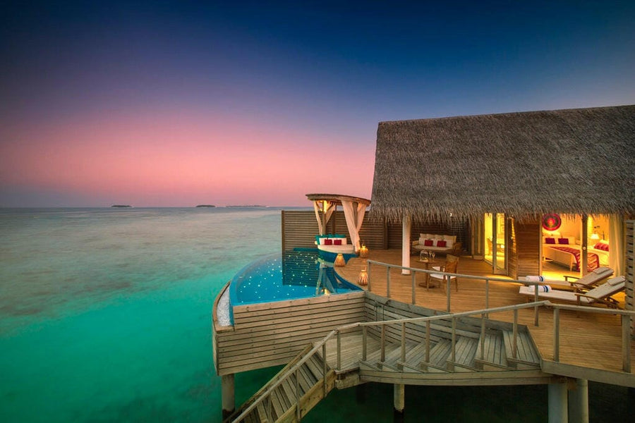 A Water Pool Villa at Milaidhoo Maldives at dusk, lit plunge pool and warm light under thatch.
