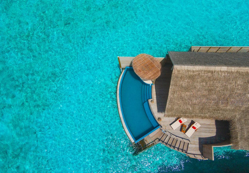 A water villa at Milaidhoo Maldives from above, crescent pool and two loungers with red towels.