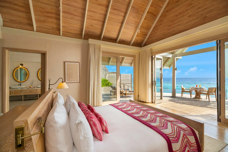 A villa bedroom at Milaidhoo Maldives, pink runner on the bed and doors to a deck over the sea.