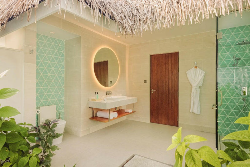 A villa bathroom at Nova Maldives, green patterned tiles, round backlit mirror and a walk-in shower.