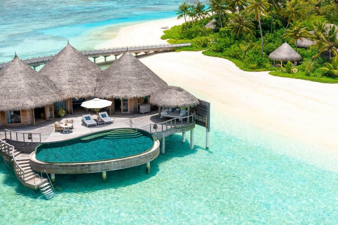 An Ocean House at The Nautilus Maldives from the air, thatched pavilions and a curved pool over the lagoon