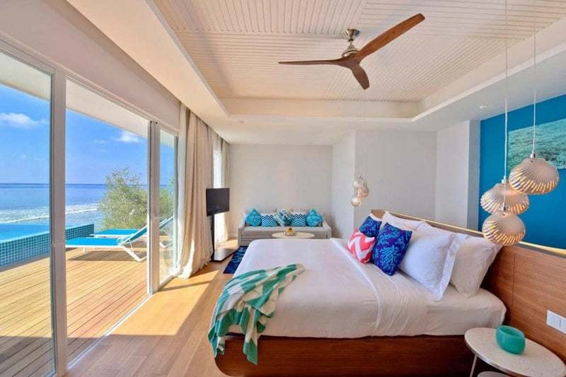 A villa bedroom at Kandima Maldives, shell pendant light and doors onto a pool deck and the sea.