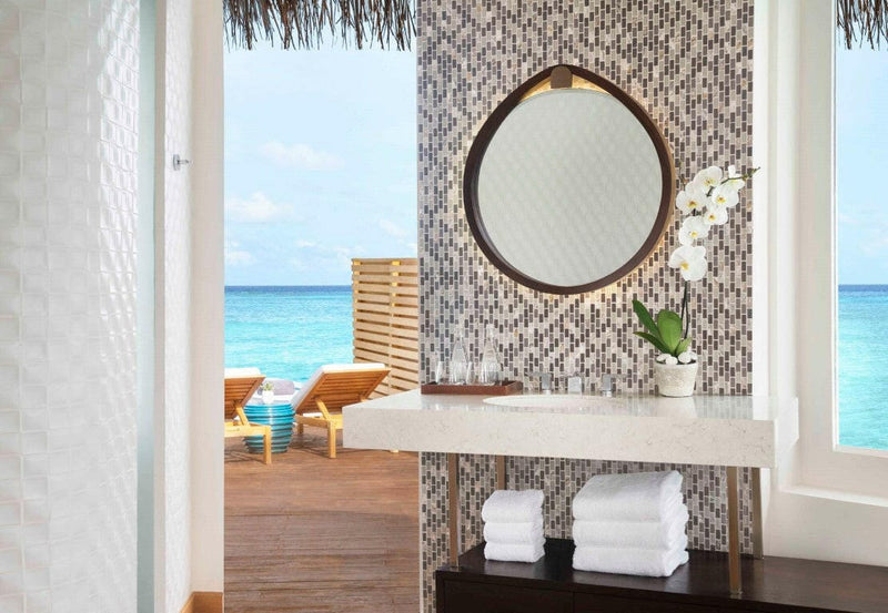 A villa bathroom vanity at JW Marriott Maldives, round gilt mirror and an orchid above folded towels.