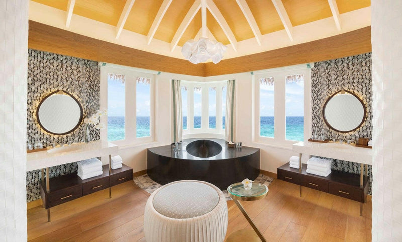 A villa bathroom at JW Marriott Maldives, dark oval tub in a bay window between two round mirrors.