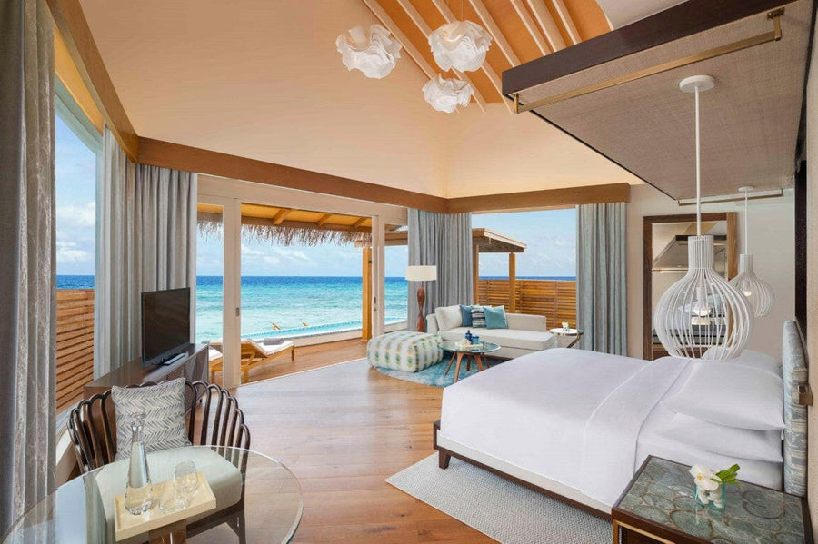 A villa bedroom at JW Marriott Maldives, cloud shaped pendant lights and glass doors onto the lagoon.