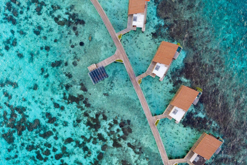 The overwater villas at Park Hyatt Maldives Hadahaa from above, copper roofs over the turquoise reef
